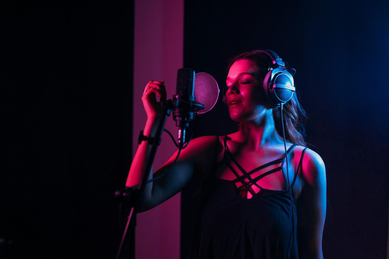 pexels-photo-7586659-7586659 Female singer with headphones singing in a dimly lit recording studio.